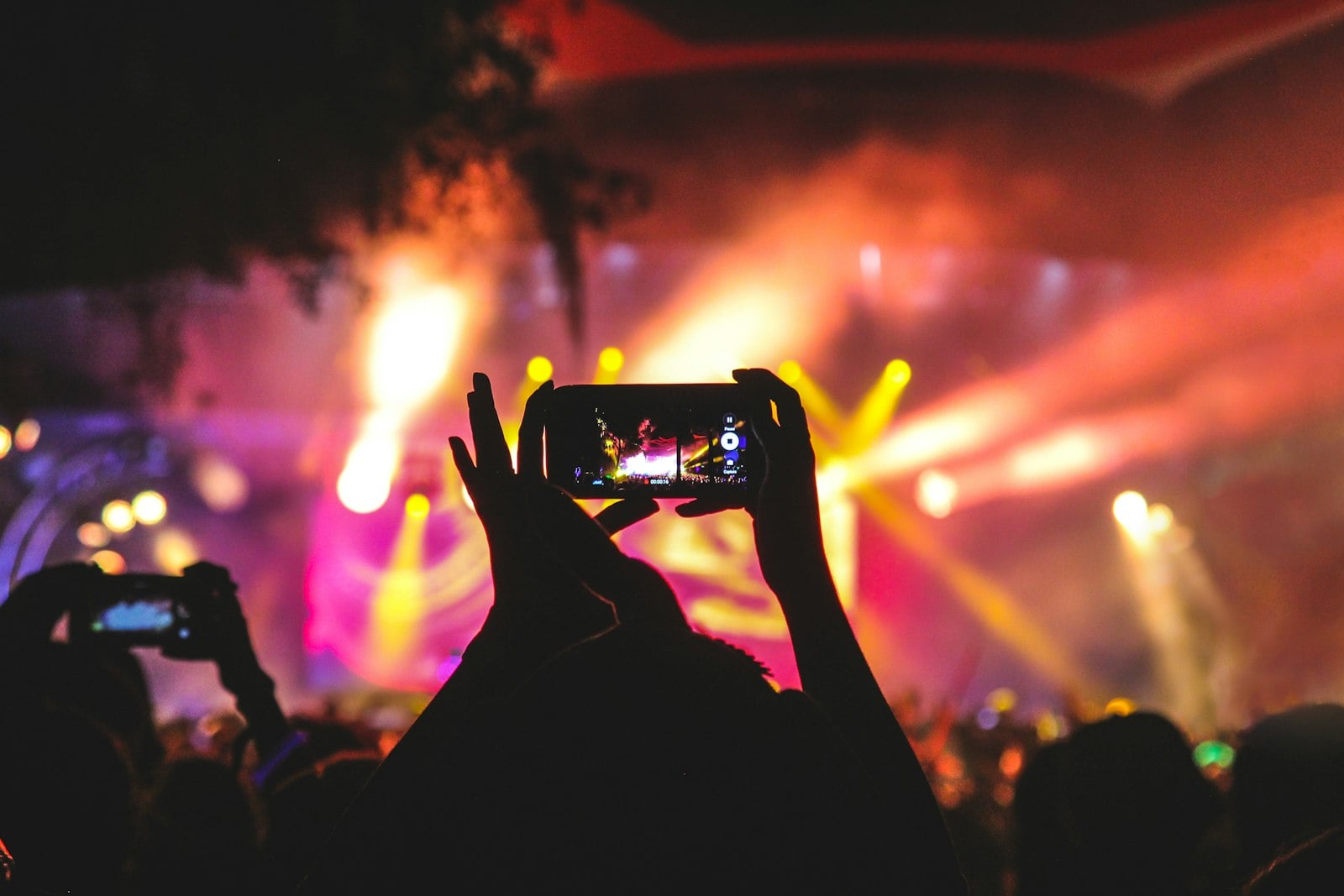 Hands holding a phone in a glowing crowd — a shared moment captured